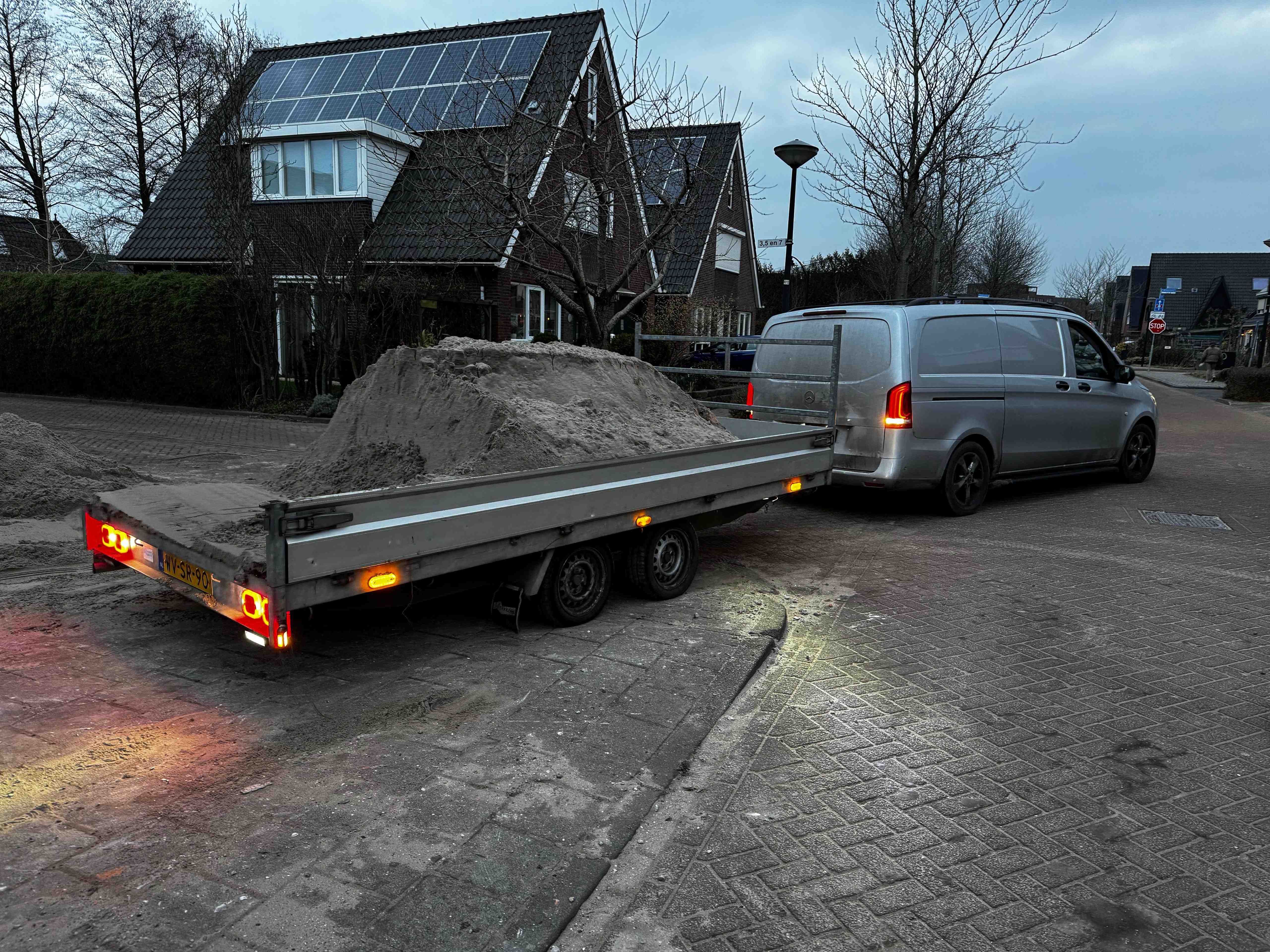 Bedrijfsbus met aanhanger vol zand in woonwijk bij schemering