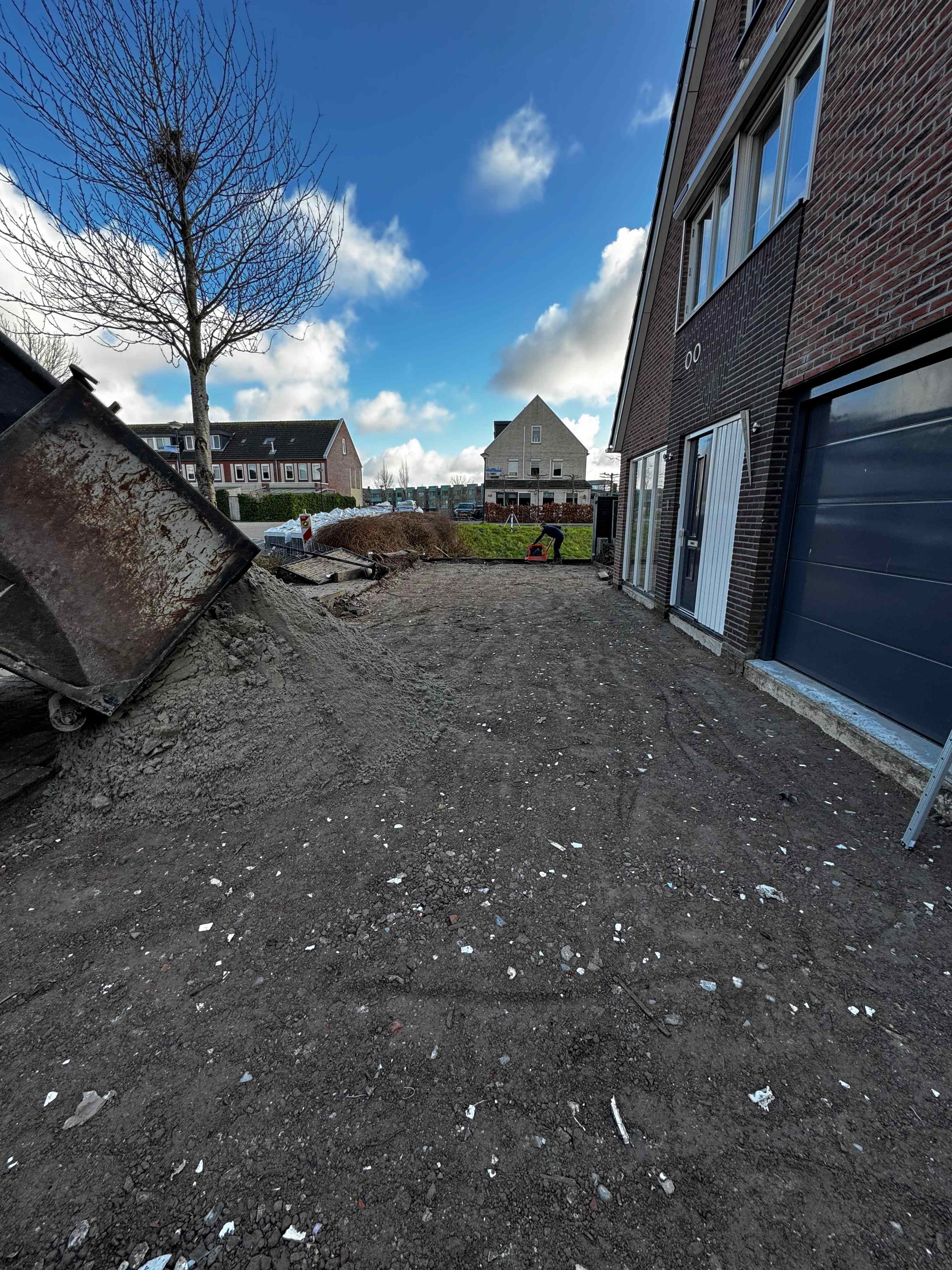 Grondwerk bij woning met container en medewerker aan het werk