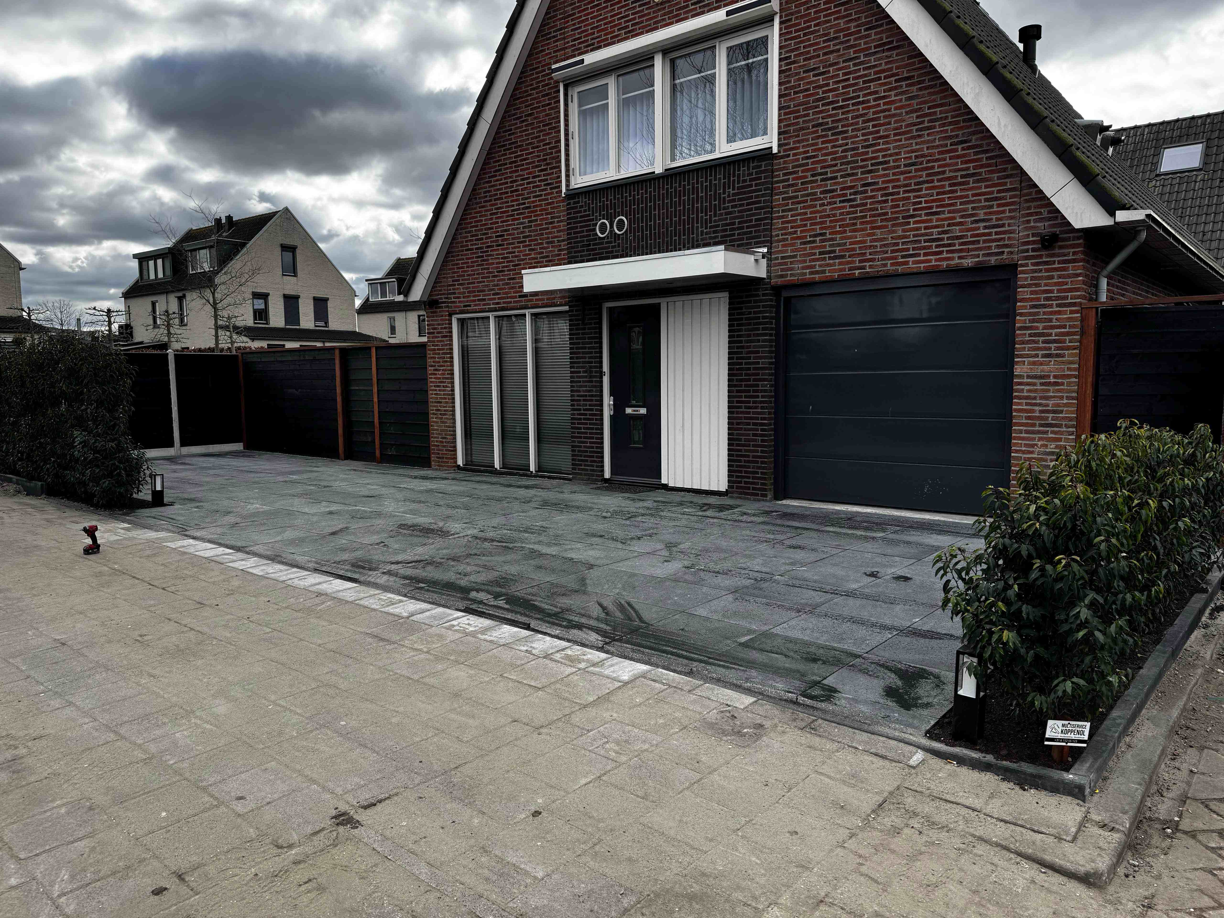 Afgewerkte oprit met nieuwe bestrating, schutting en Koppenol bordje