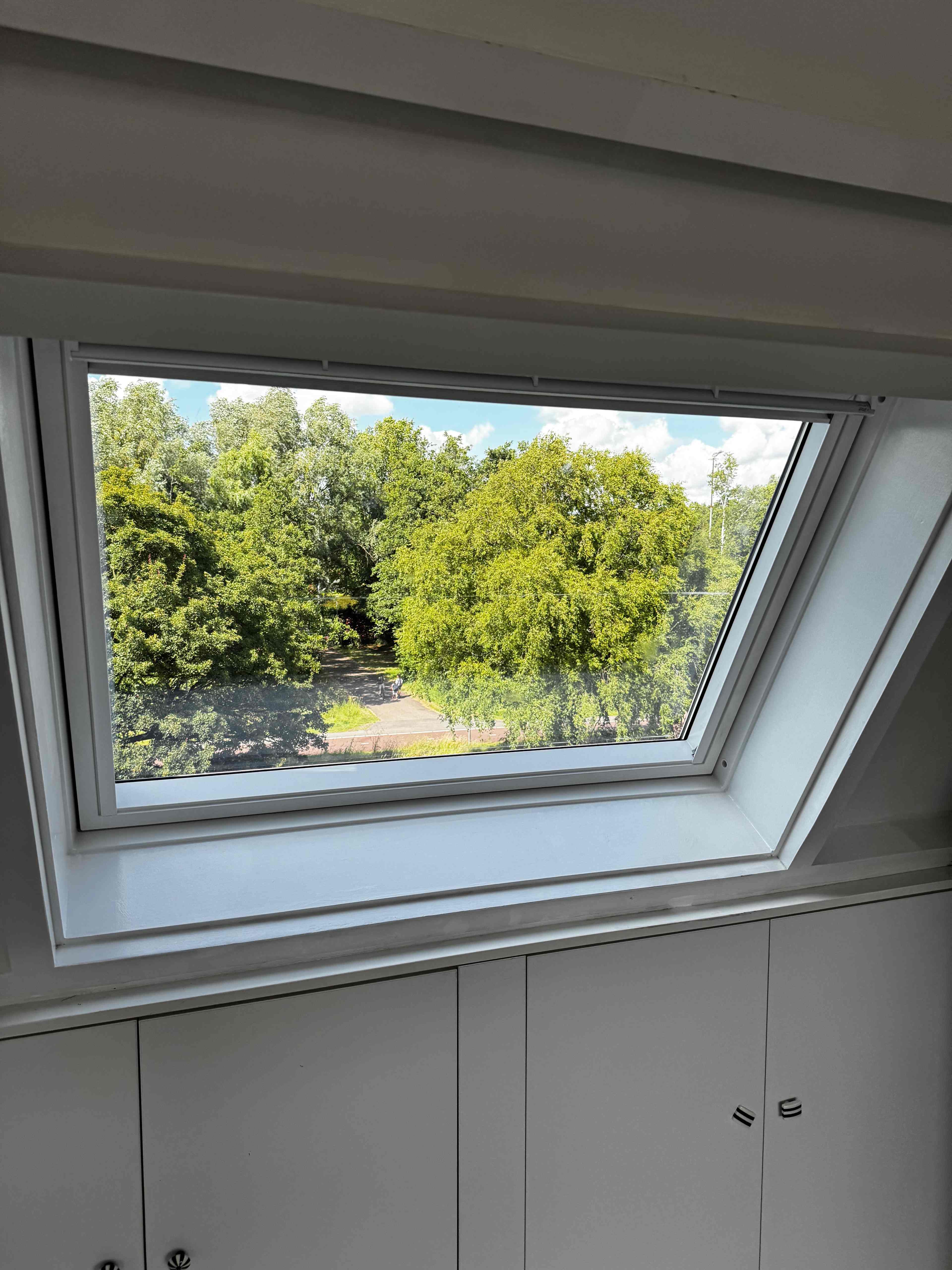 Wit dakraam geopend met uitzicht op bomen boven inbouwkasten