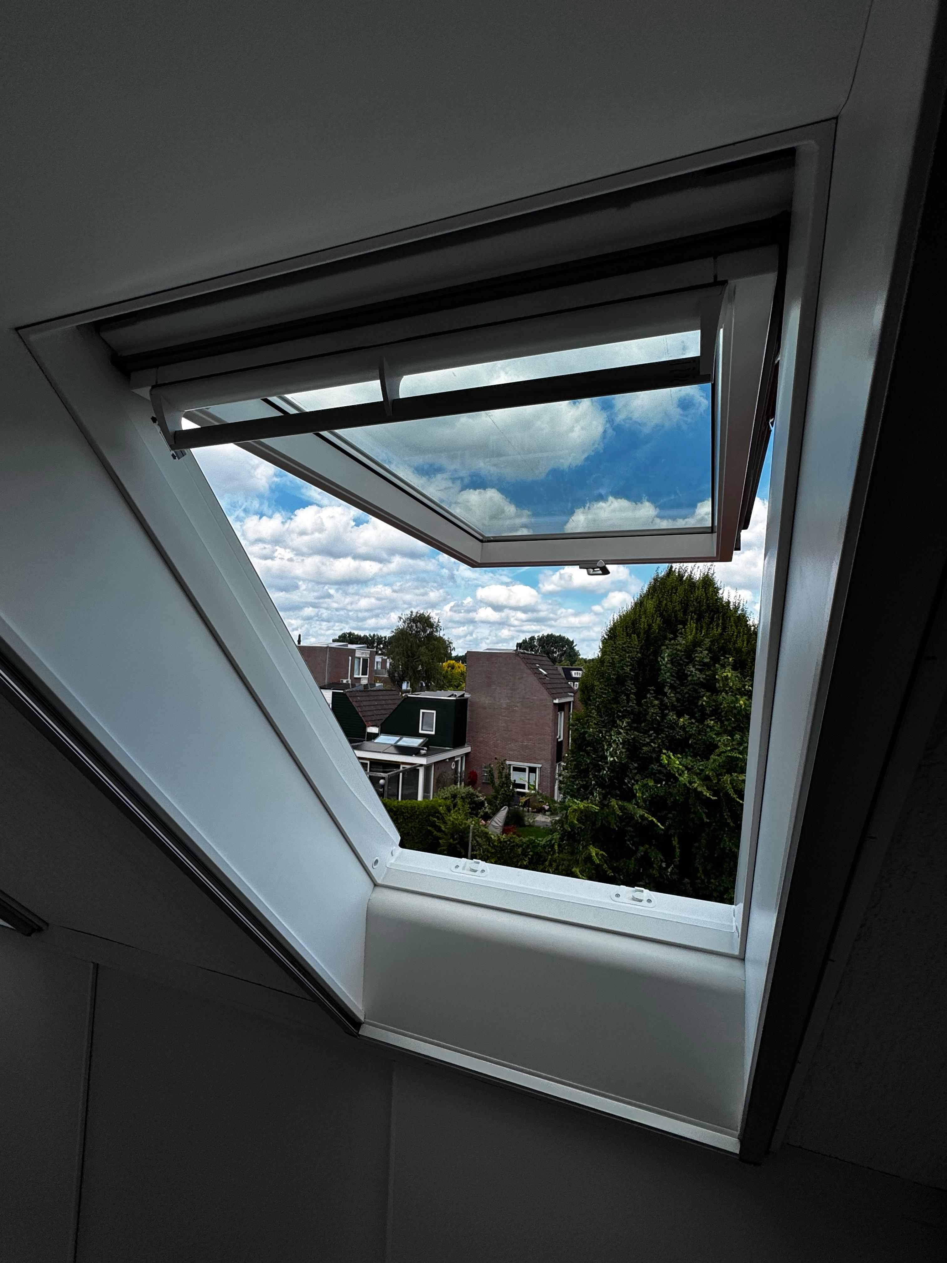 Wit dakraam geopend met uitzicht op woonwijk en blauwe lucht