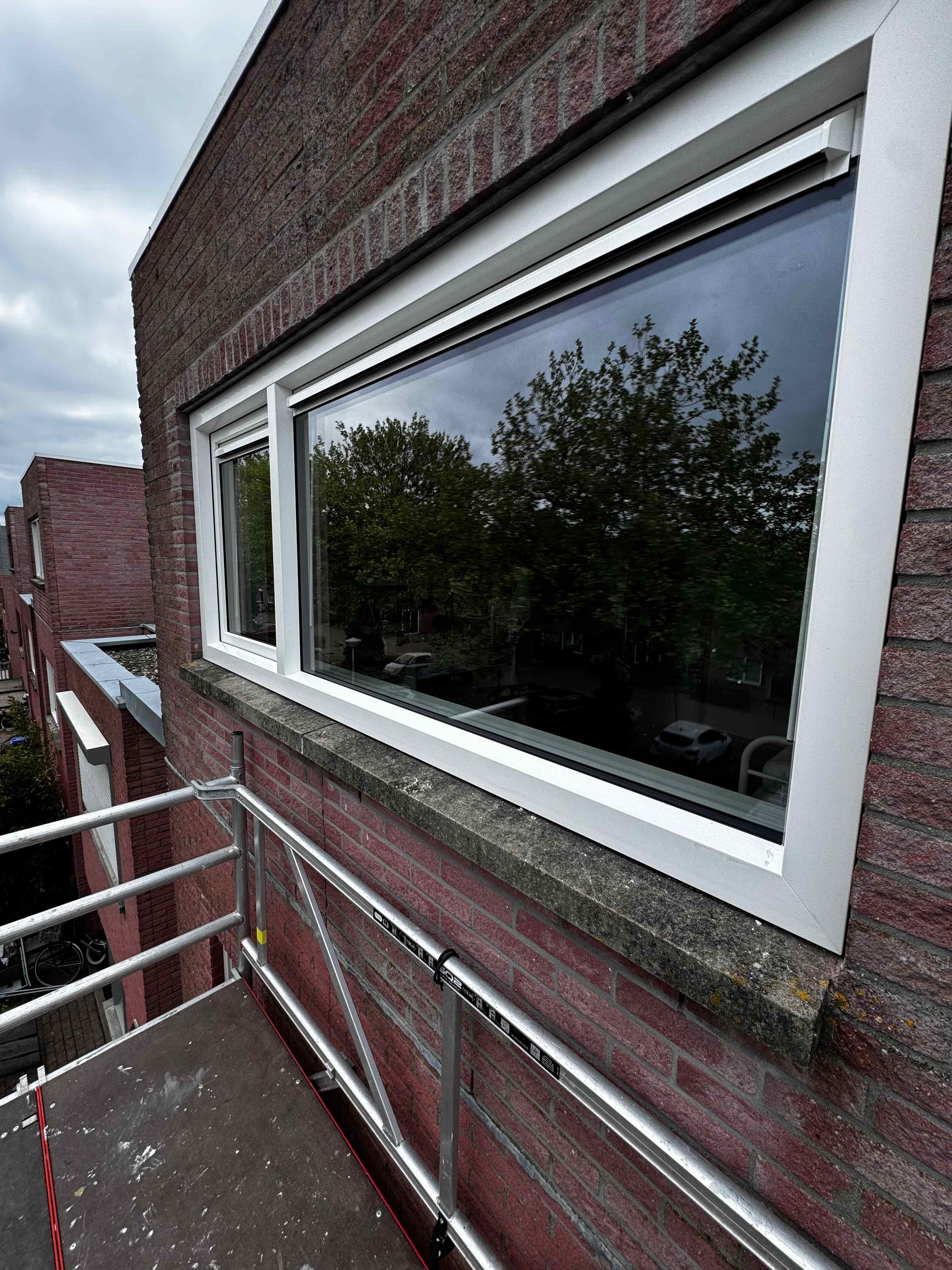 Nieuw wit kunststof kozijn geplaatst in bakstenen gevel vanaf steiger