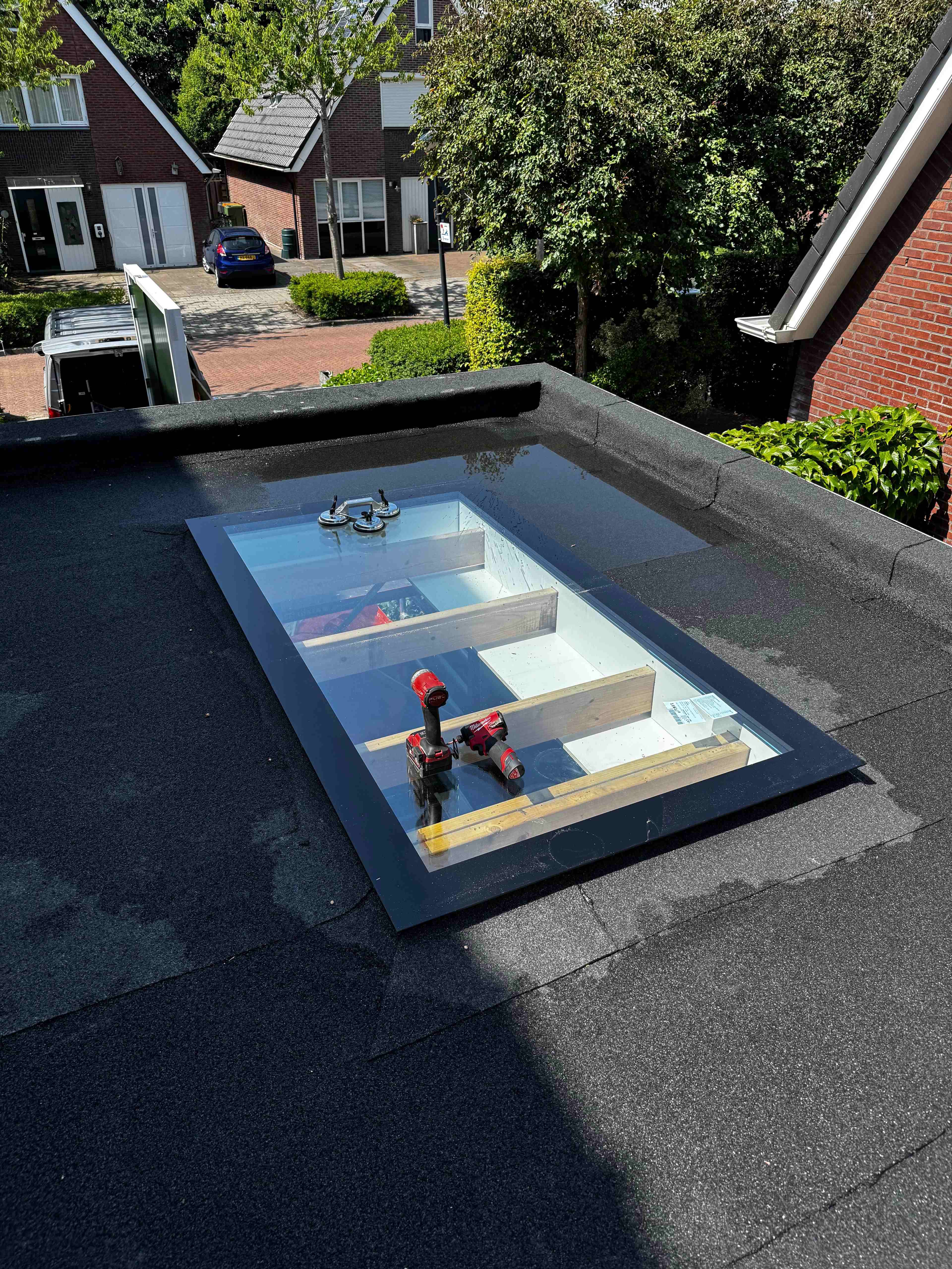 Grote lichtkoepel tijdens montage op bitumen platdak in woonwijk