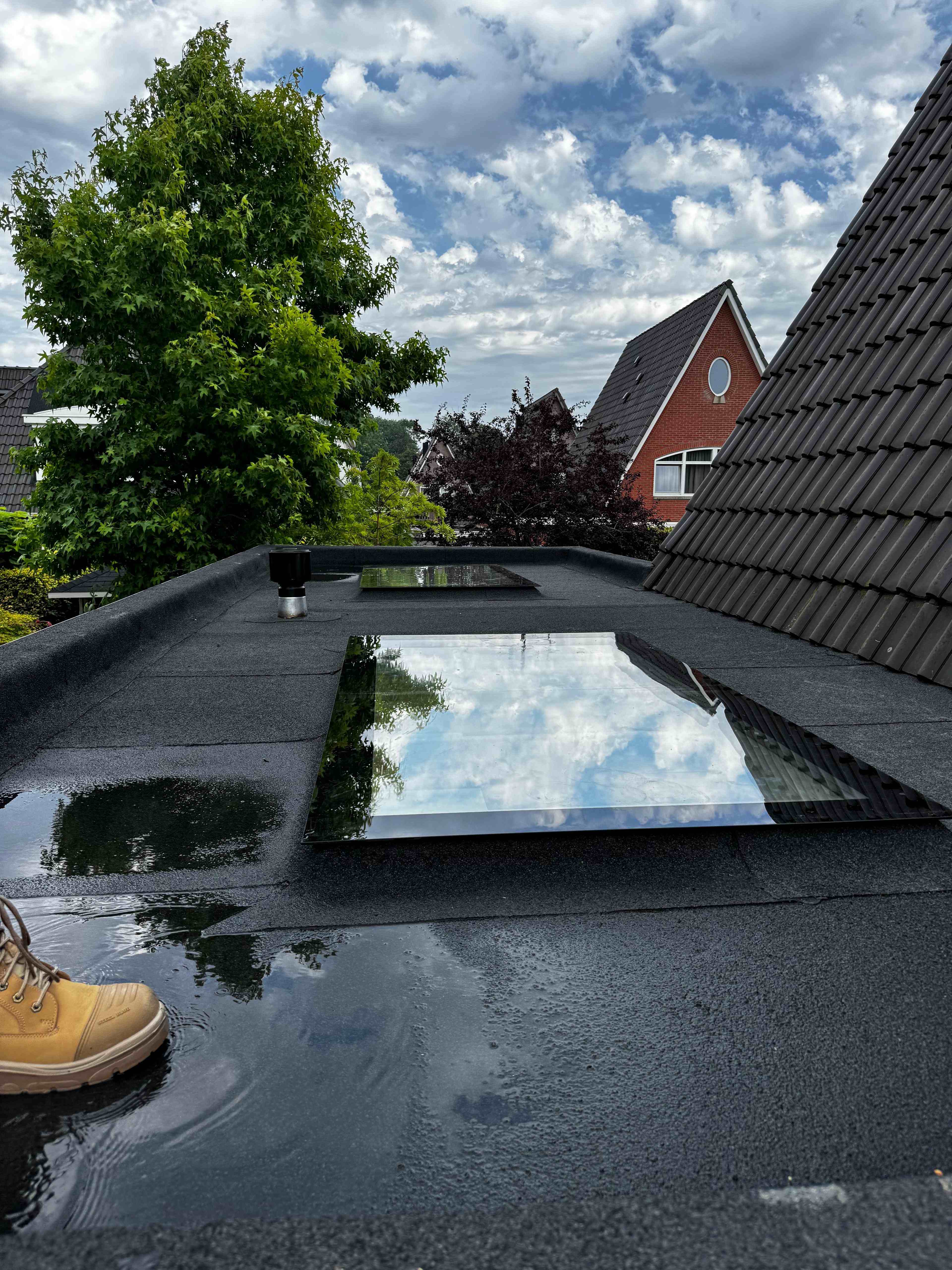 Vlakke lichtkoepels in plat dak met wolkenspiegeling en bitumen