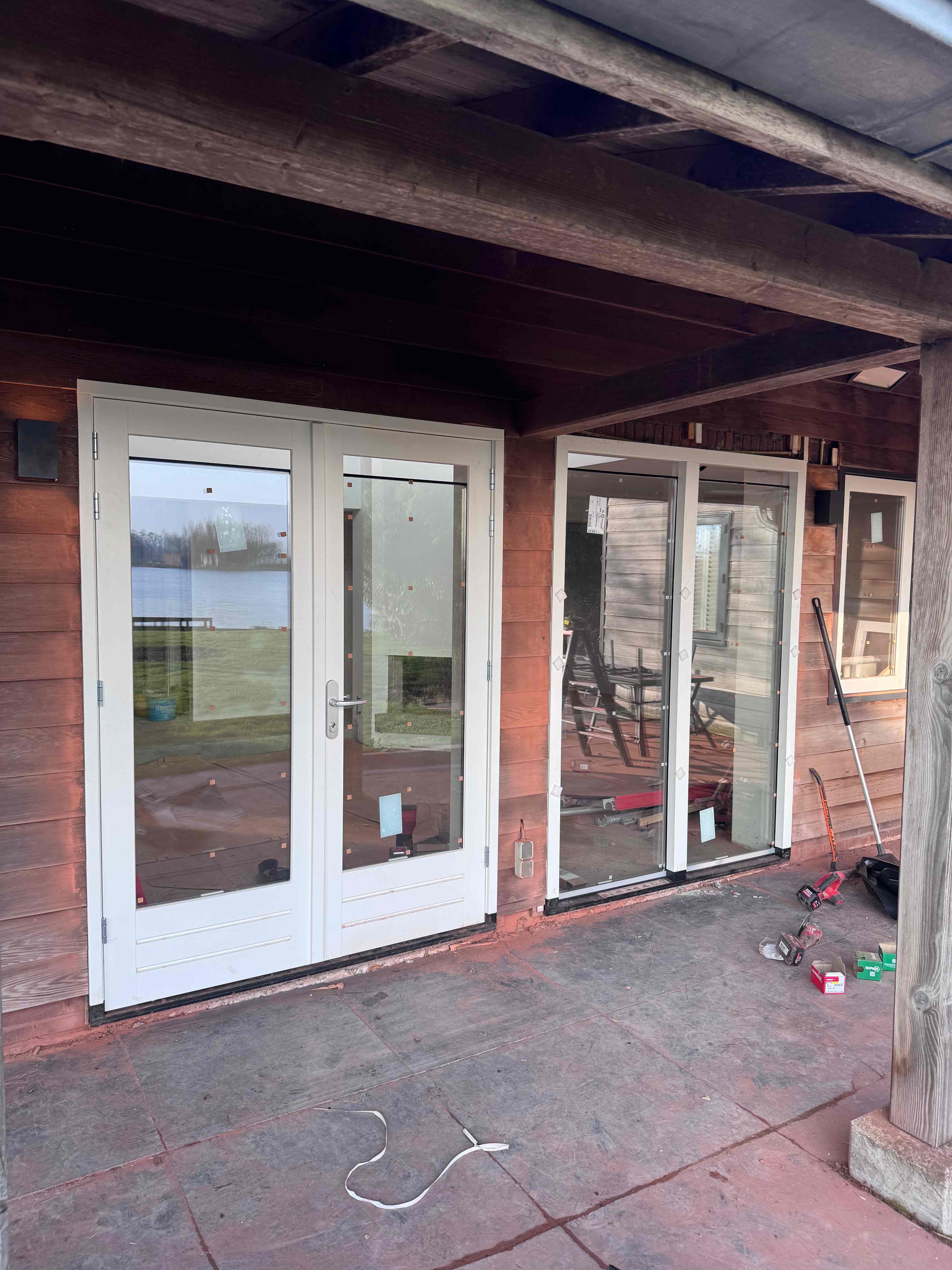 Witte kunststof openslaande deuren en schuifpui geplaatst in houten woning aan het water