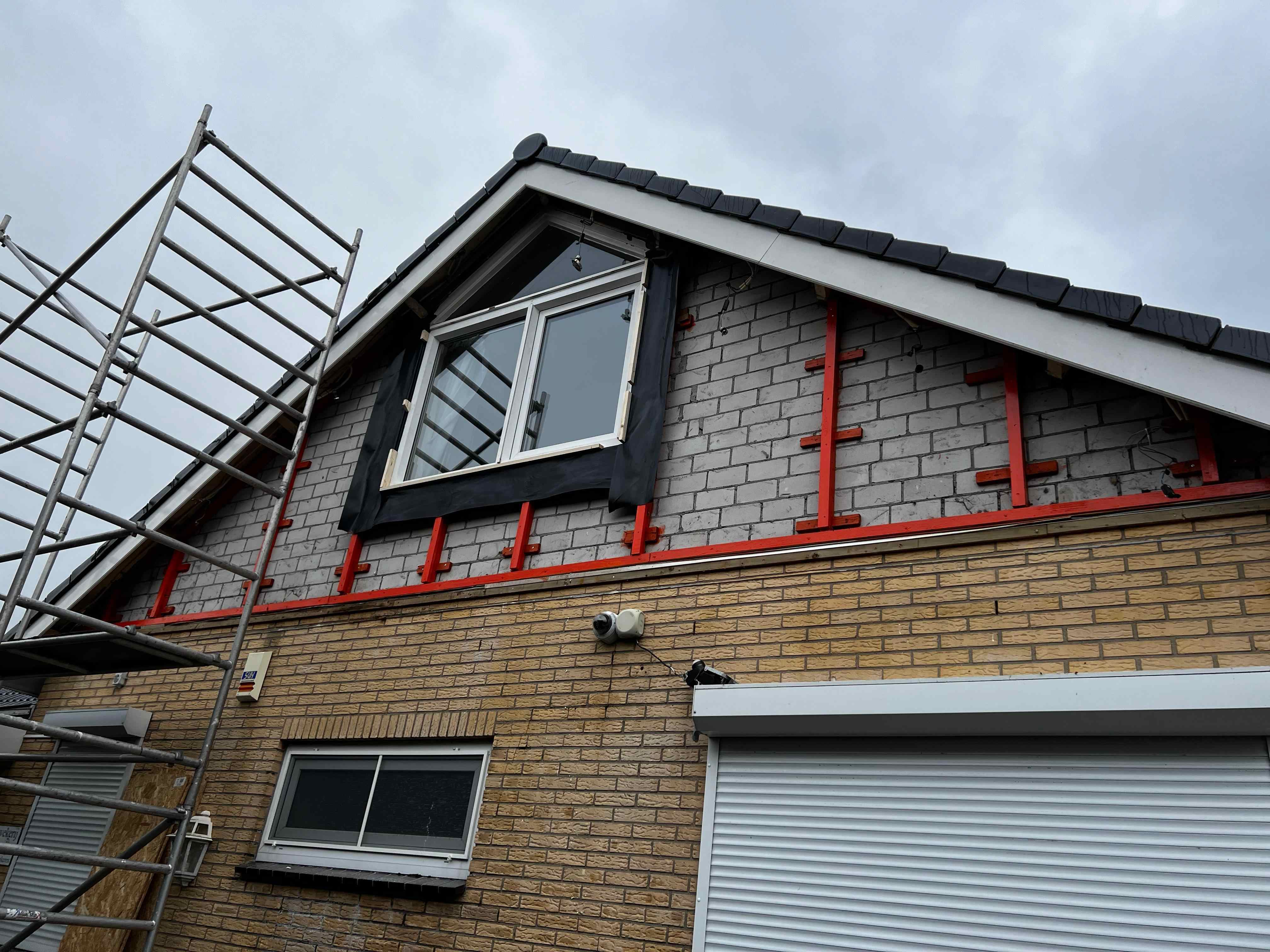 Gevelbekleding in aanbouw met rode montageprofielen en steiger