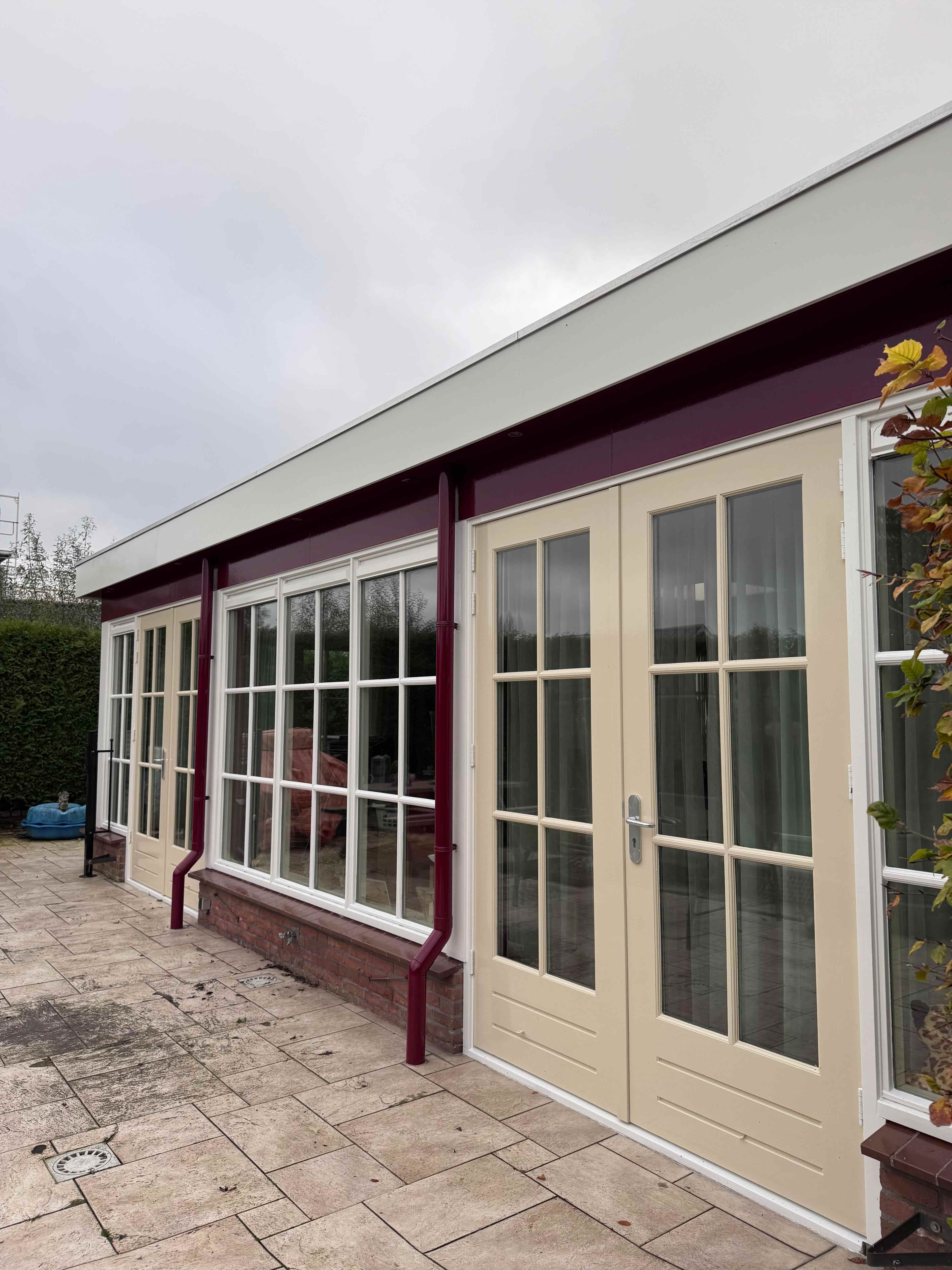 Serre met geschilderde openslaande deuren en bordeauxrode regenpijpen