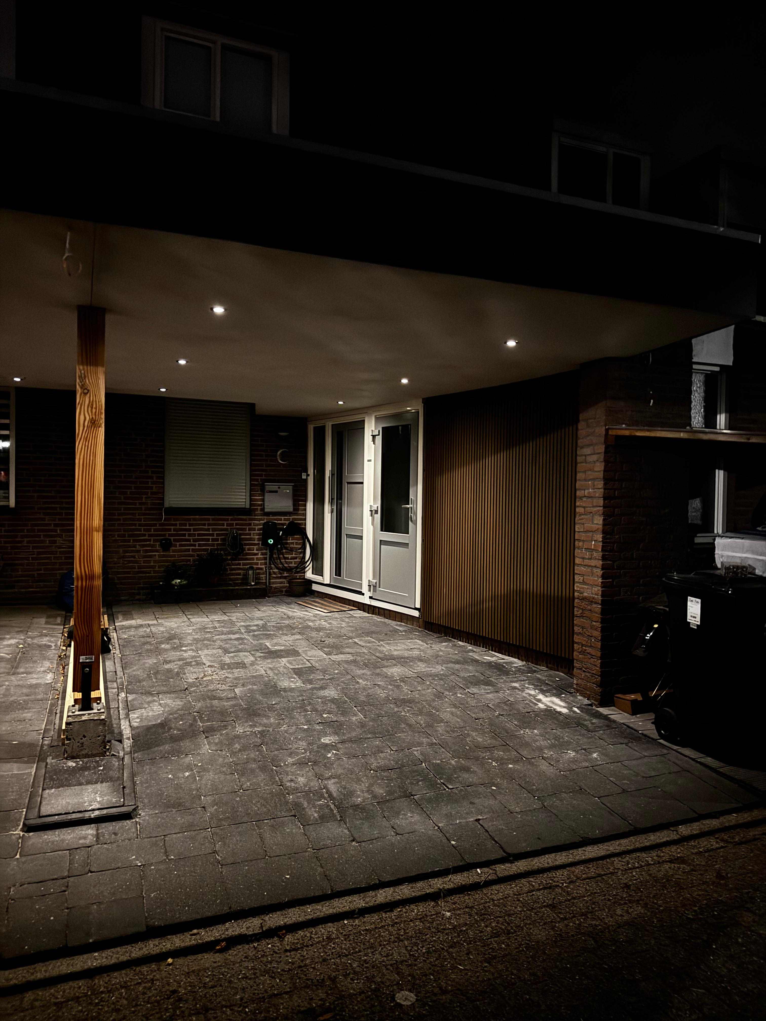 Overkapping met inbouwspots en houten gevelbekleding bij nacht