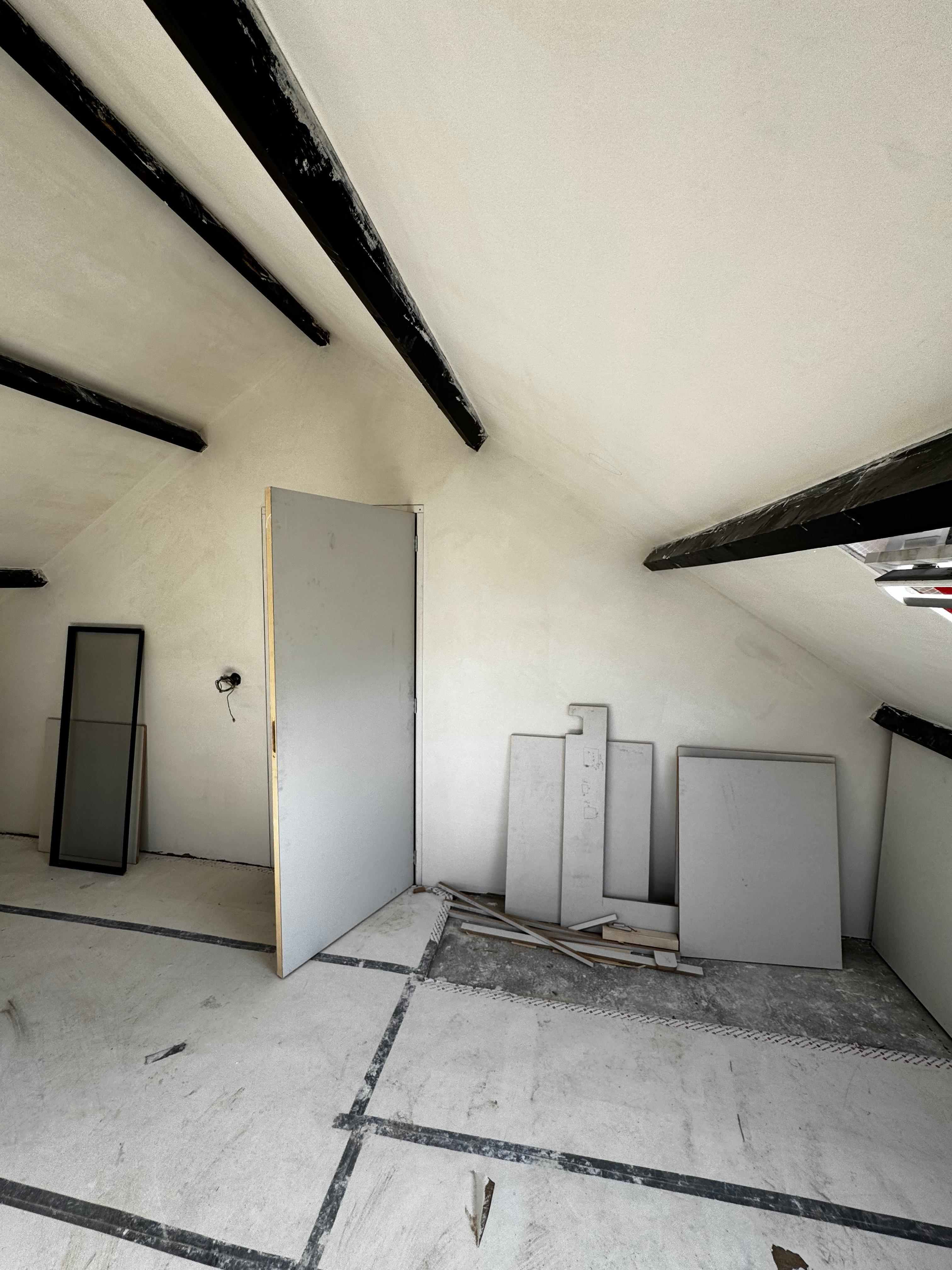 Zolderruimte met donkere balken, nieuw stucwerk en deurpanelen