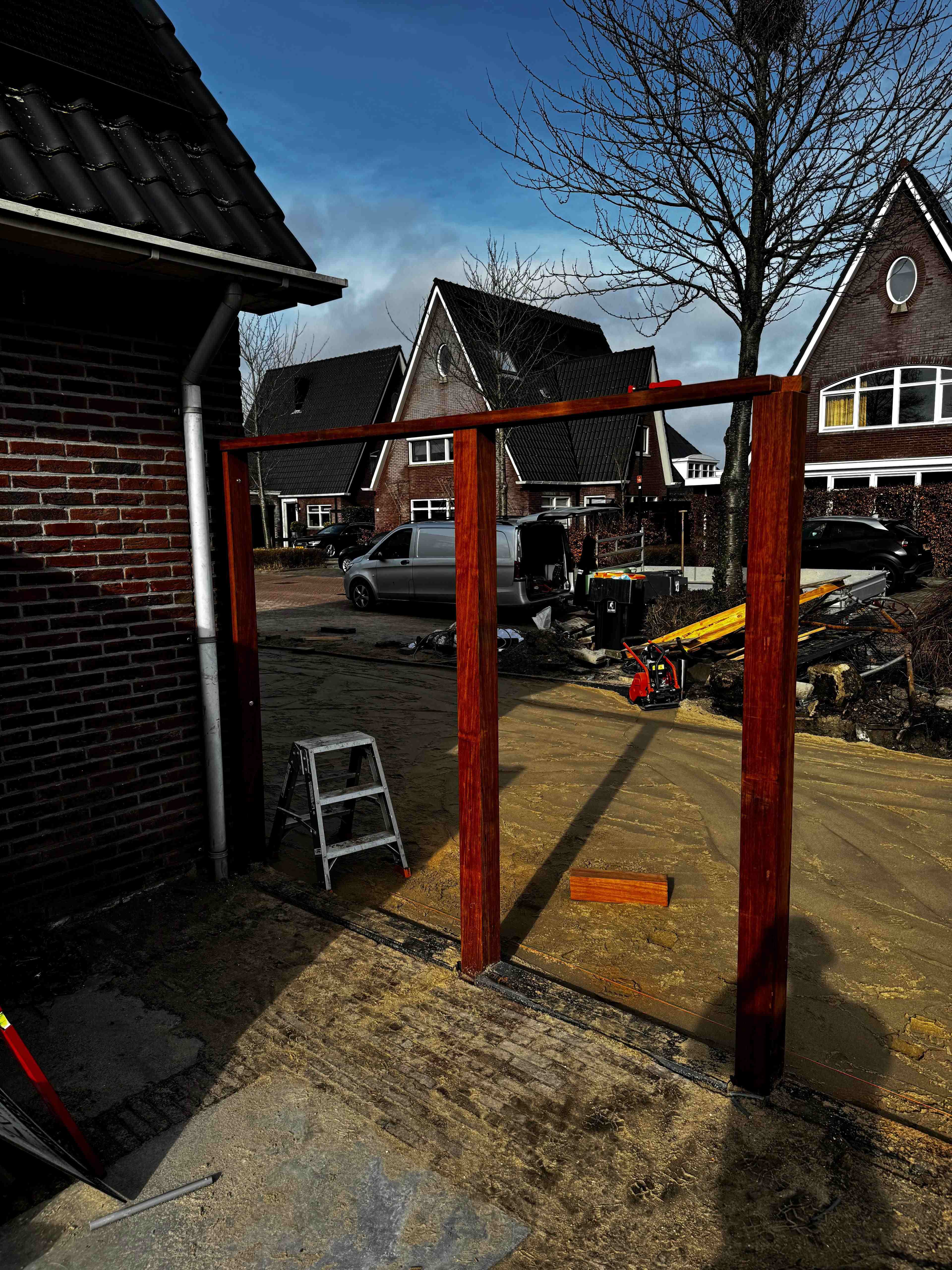 Hardhouten pergola frame in aanbouw op zandbed met bedrijfsbus