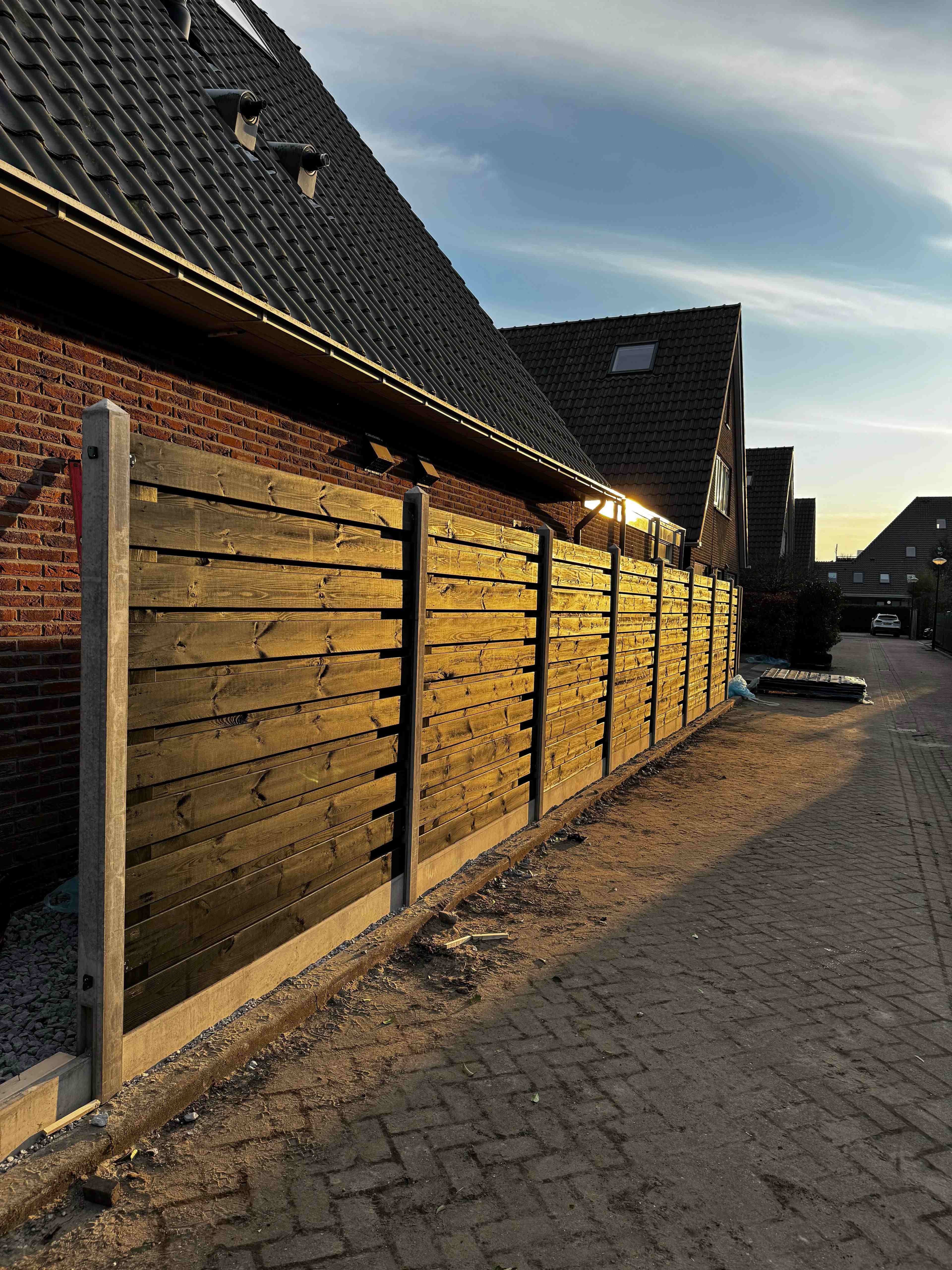 Nieuwe houten schutting met betonpalen langs woning bij zonsondergang