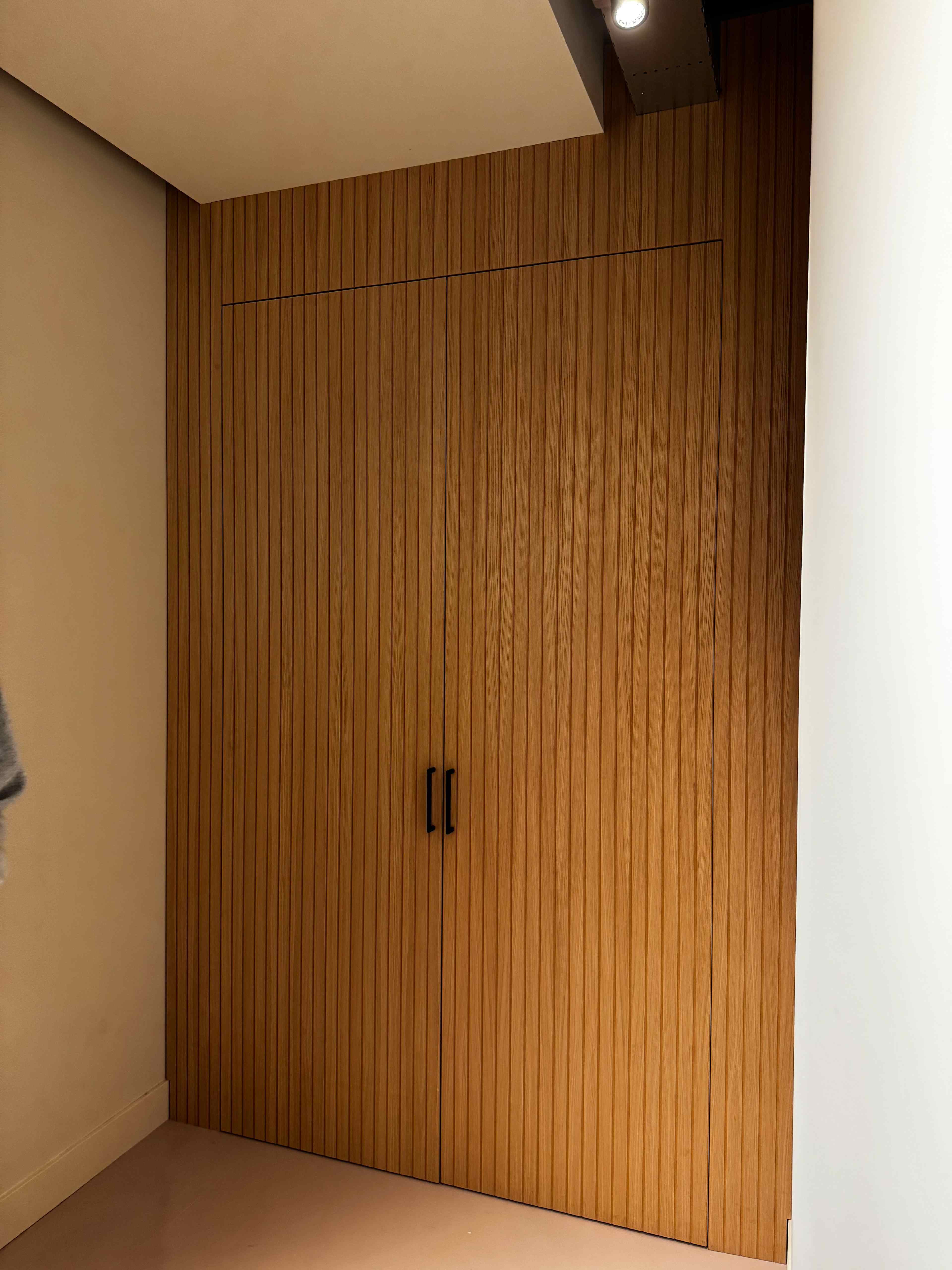 Inbouwkast op maat met verticale houten latten en zwarte handgrepen