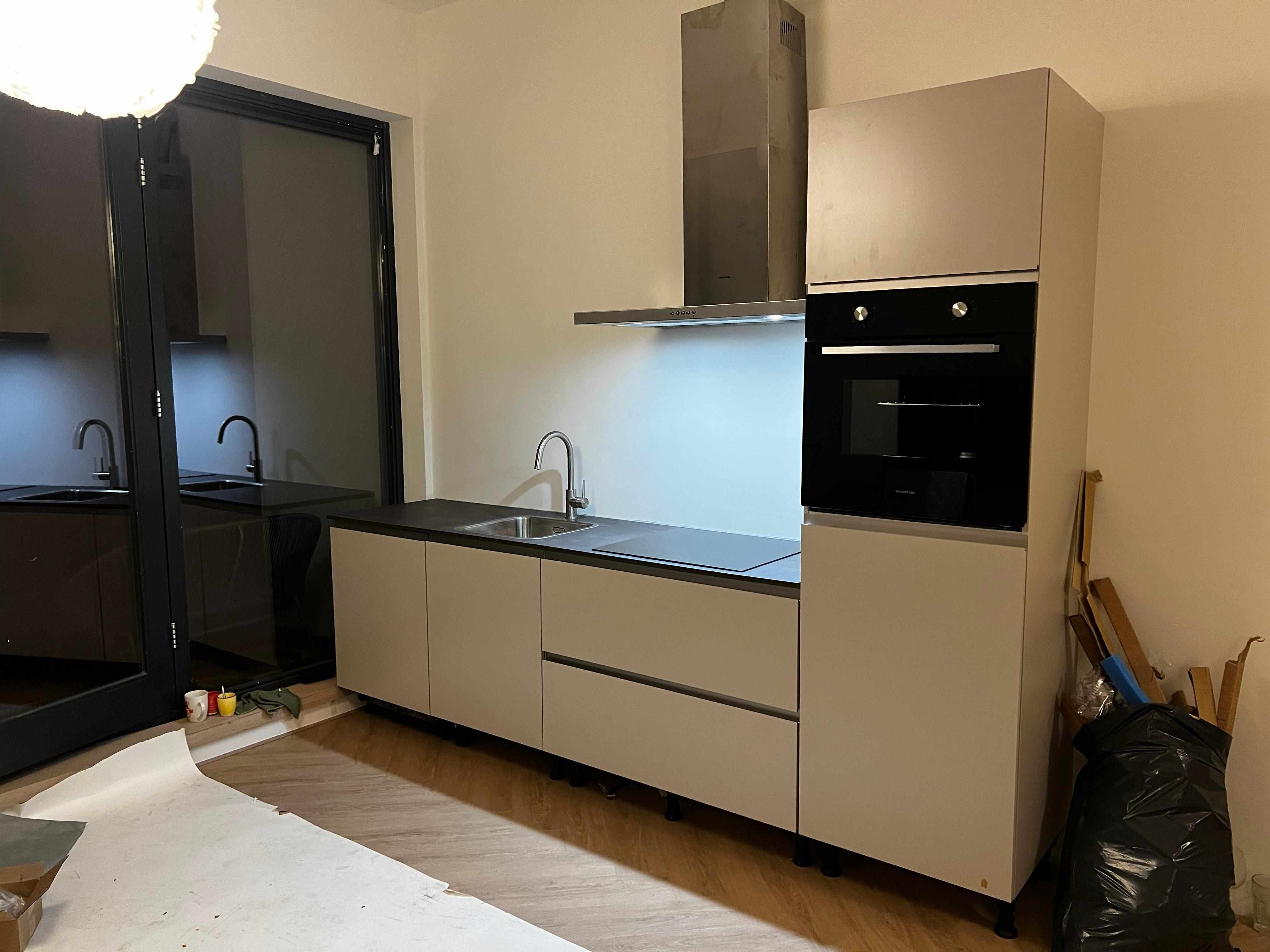 Moderne keuken installatie met beige kasten en zwart werkblad