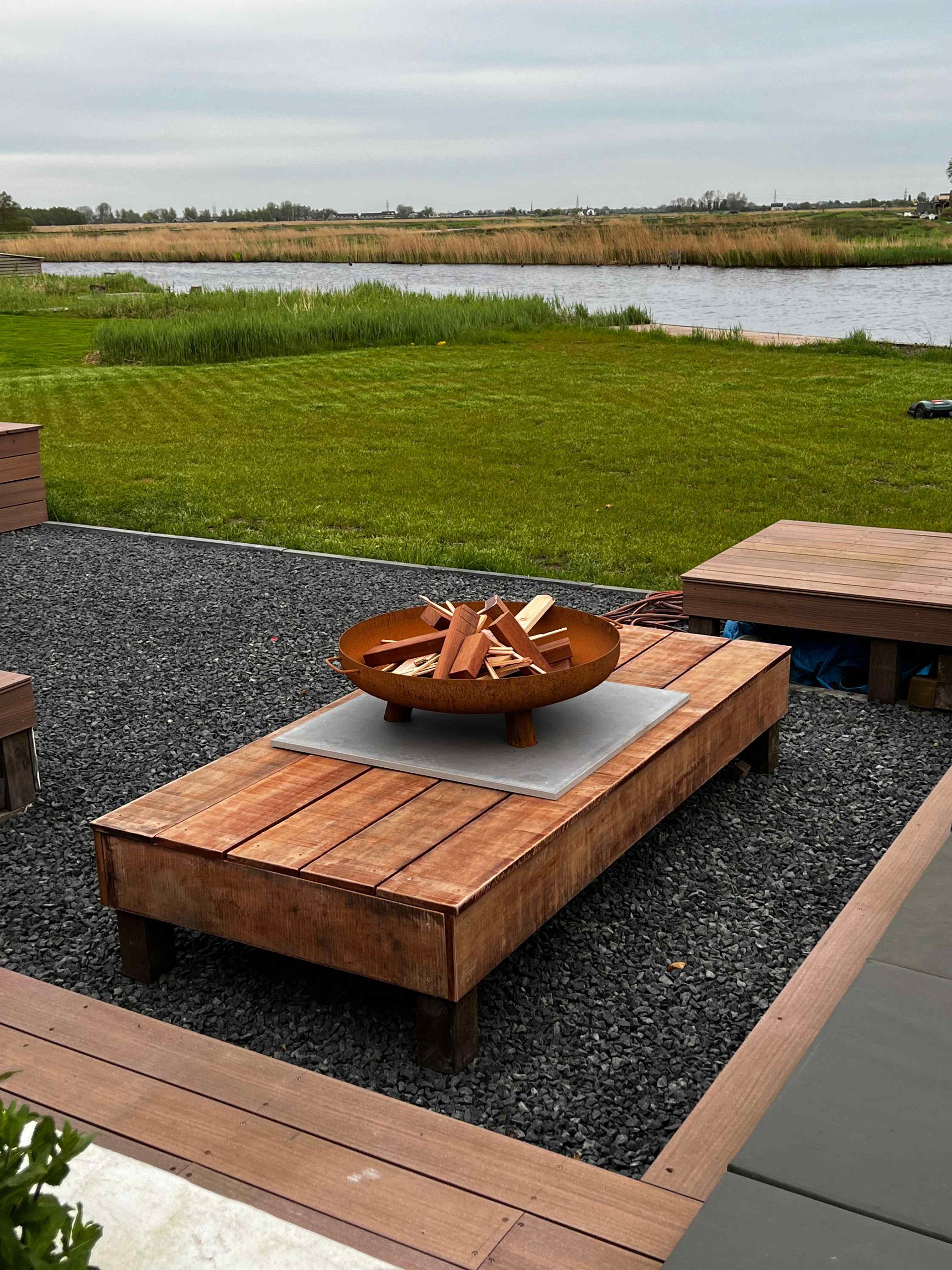 Hardhouten buitenbank met cortenstaal vuurschaal aan het water