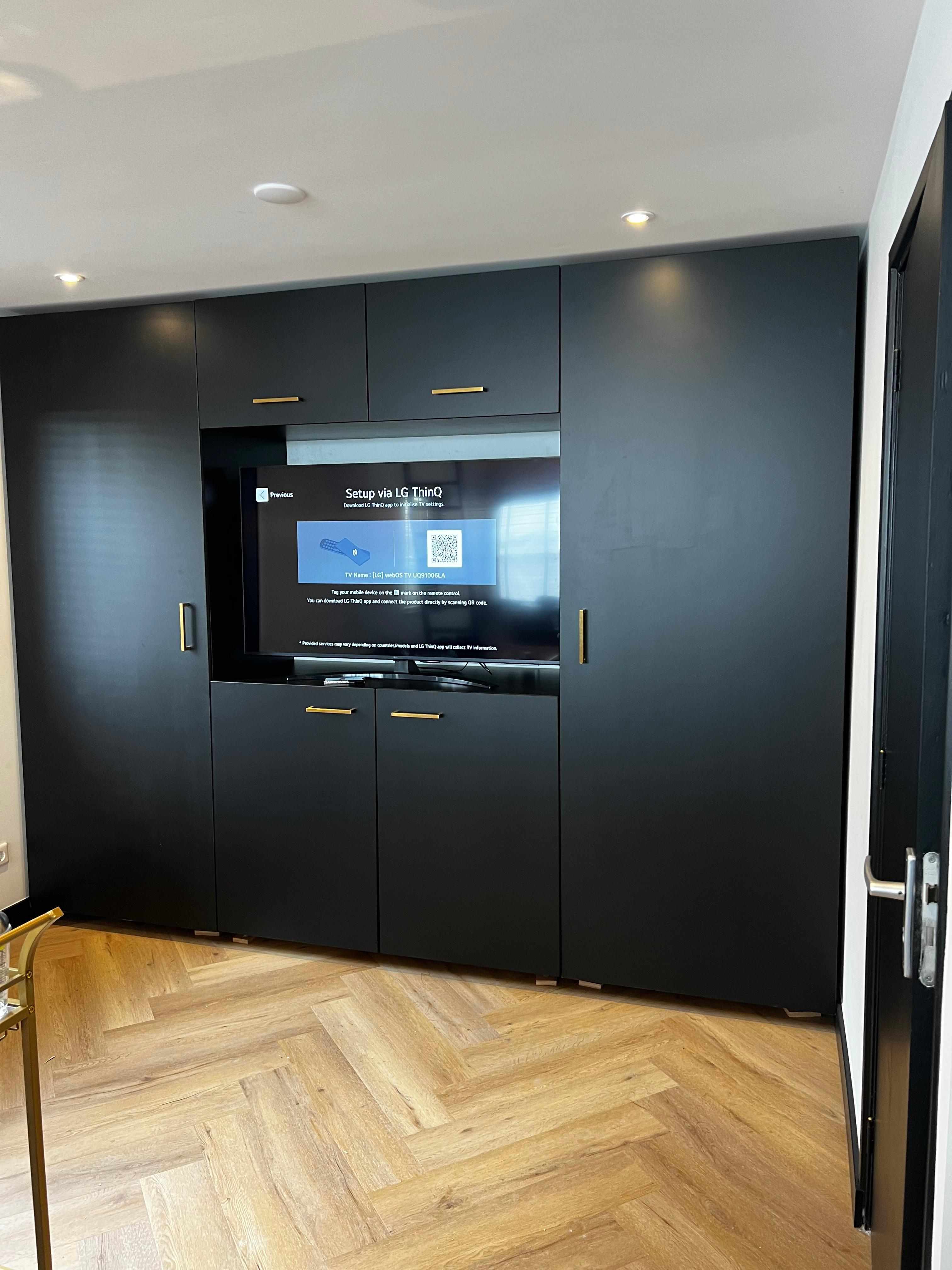 Zwarte inbouwkast met TV en gouden handgrepen, deuren dicht