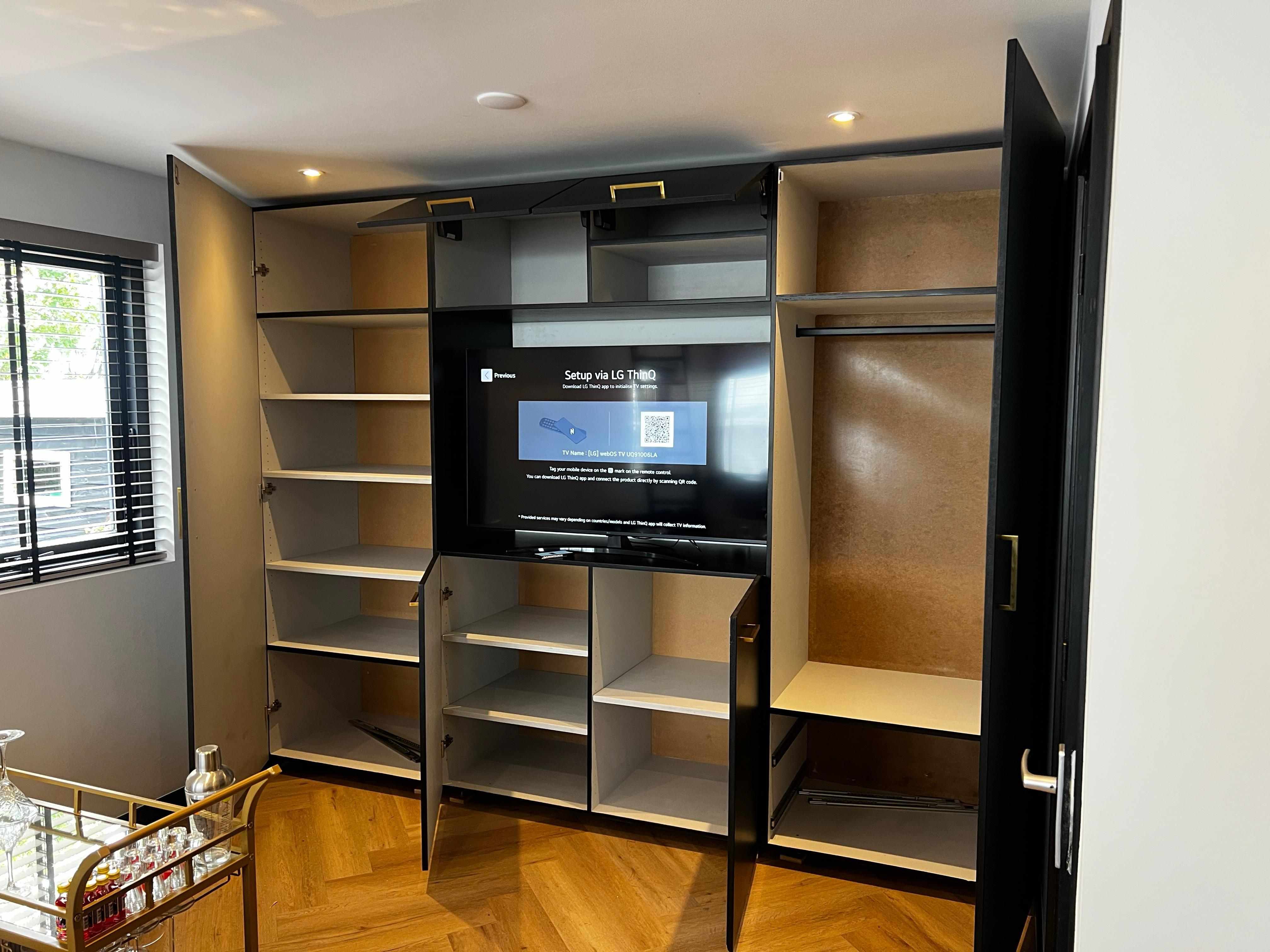 Zwarte inbouwkast met TV en gouden handgrepen, deuren open