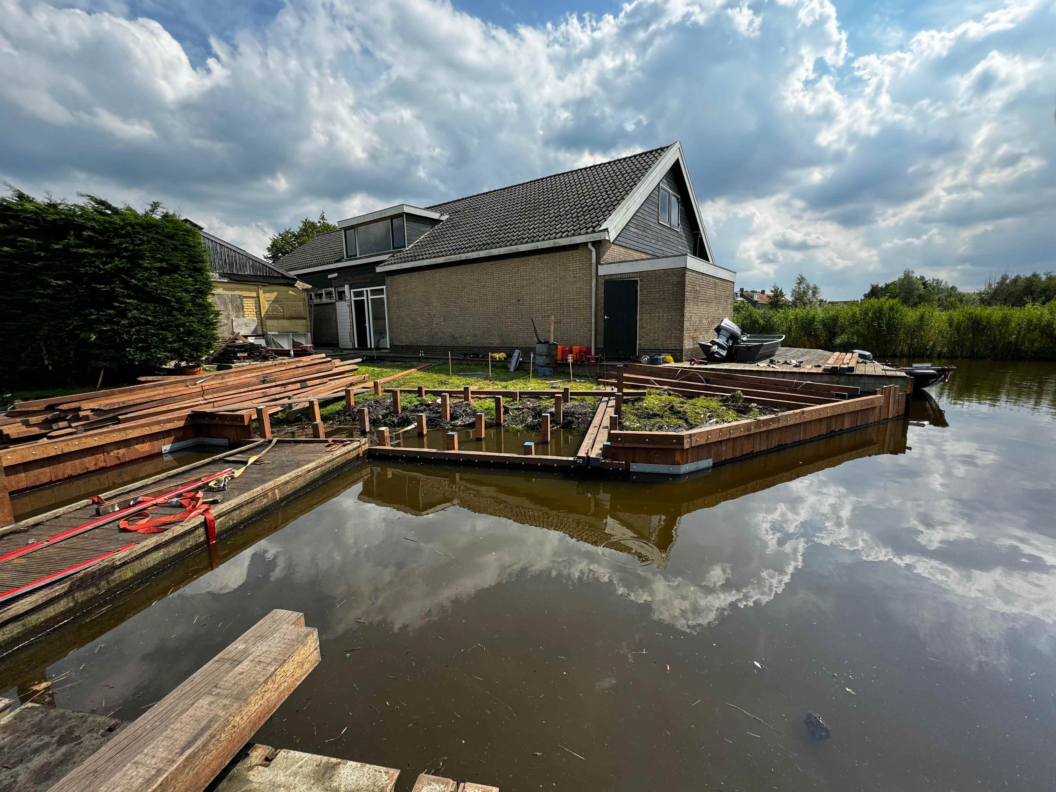 Beschoeiing en steiger in aanbouw met hardhouten balken bij woning aan het water