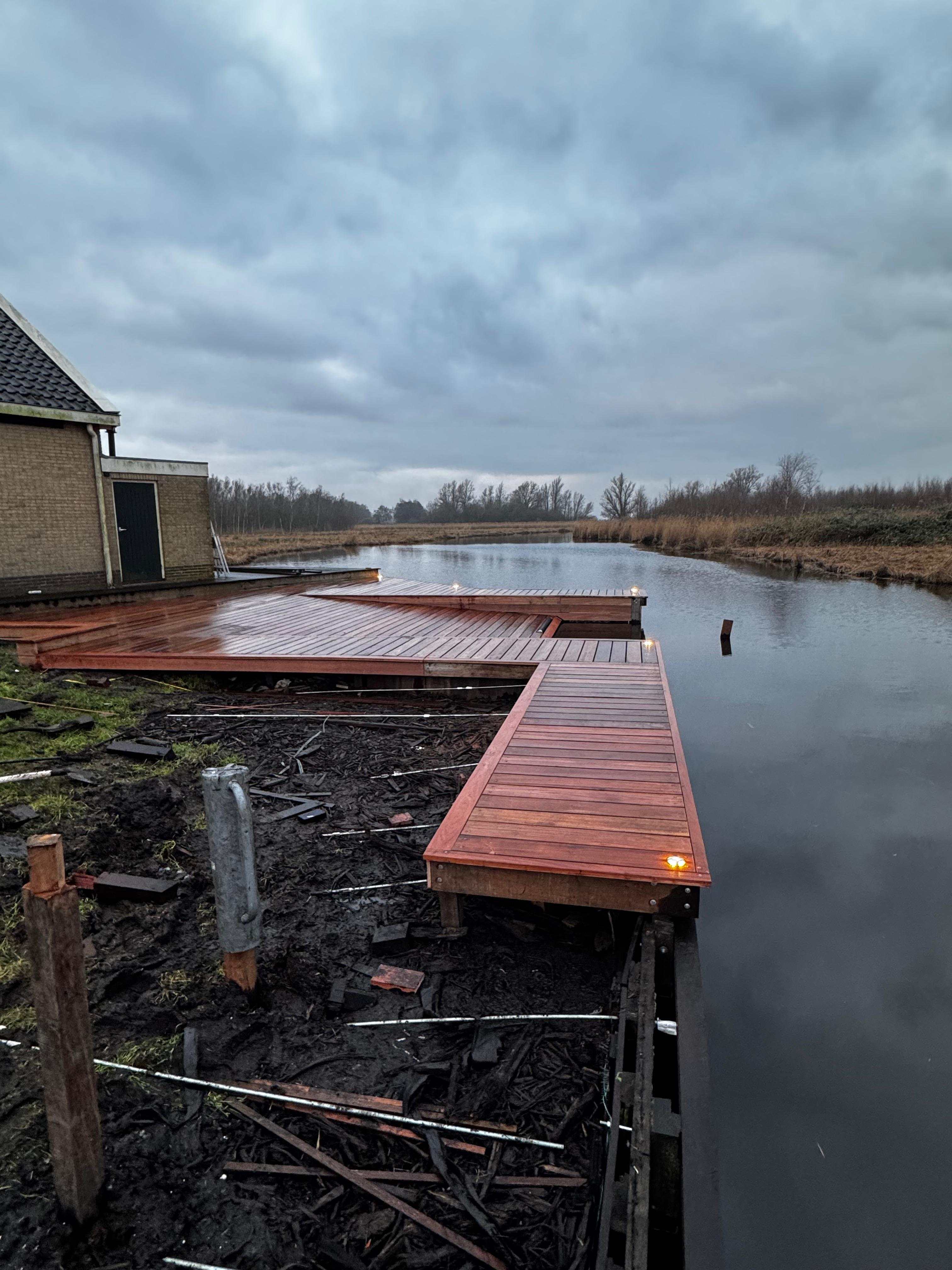 Hardhouten vlonder met inbouwverlichting aan het water in de schemering